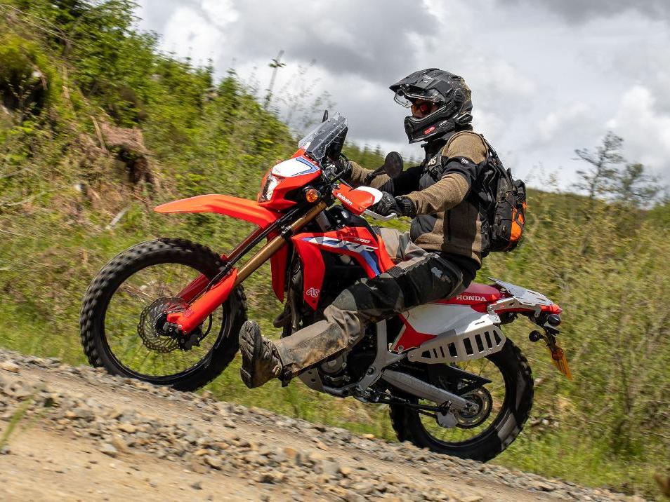 rider with leg out riding red honda crf 300l fast around a dirt road corner